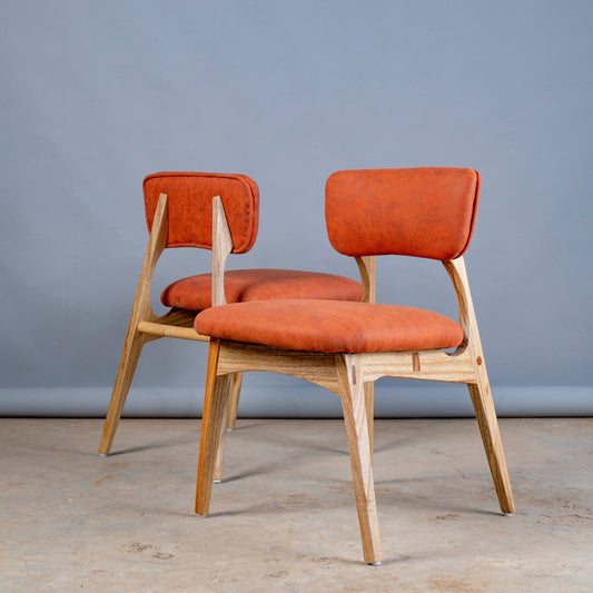 Two orange chairs with wooden frames on a gray floor and background