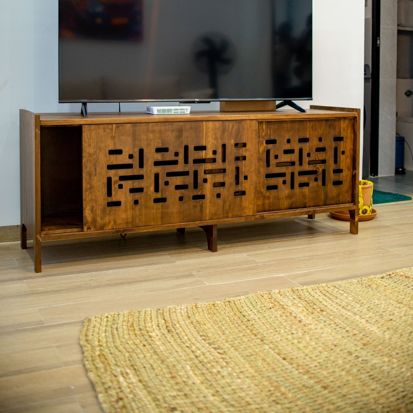 Wooden TV stand with a television on it in a room with a rug and door.