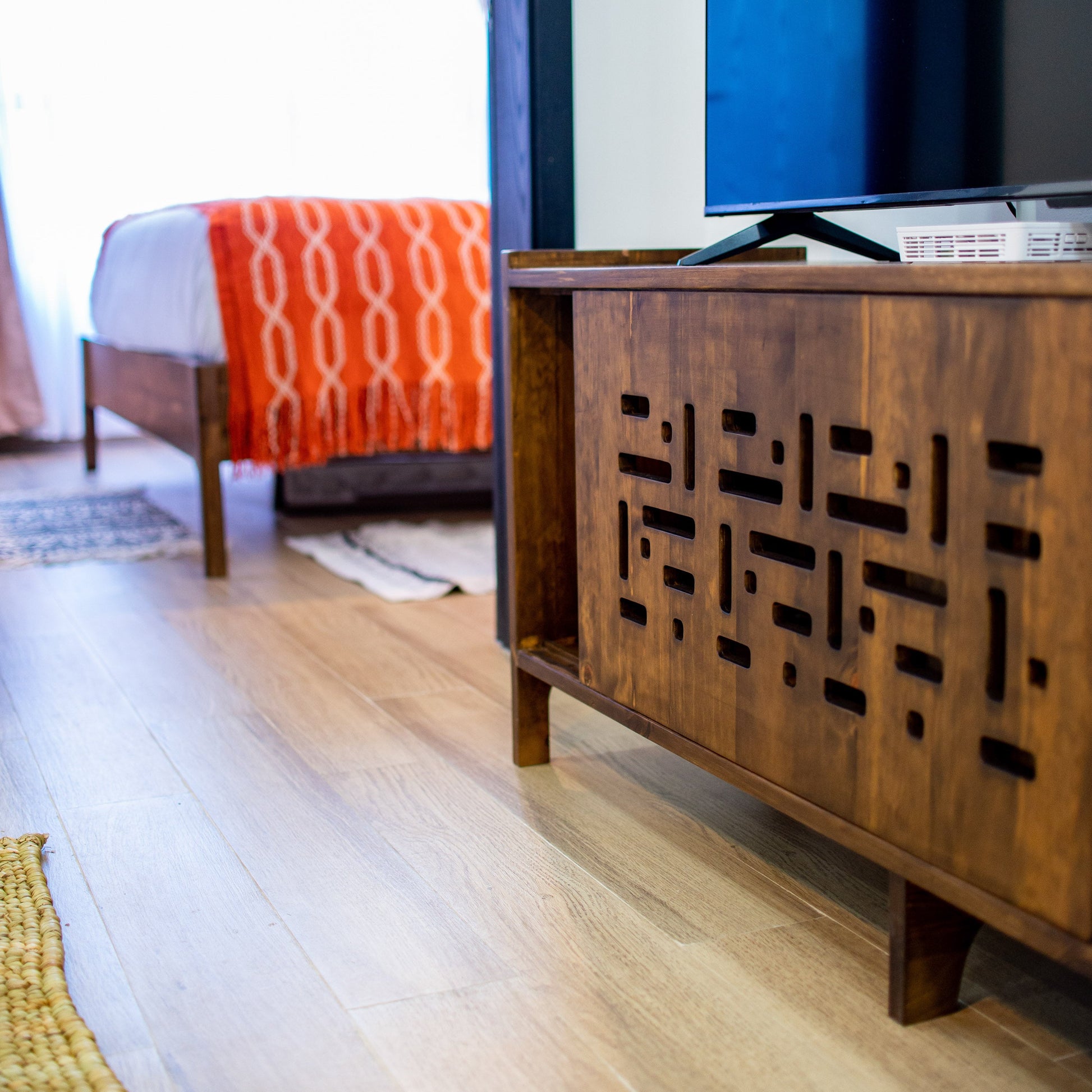 Wooden entertainment console with a television in a room with a bed and window.