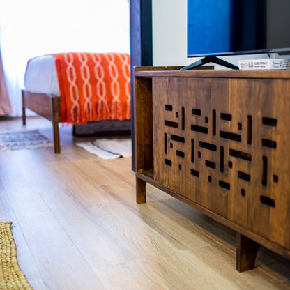 Wooden entertainment console with a television in a room with a bed and window.