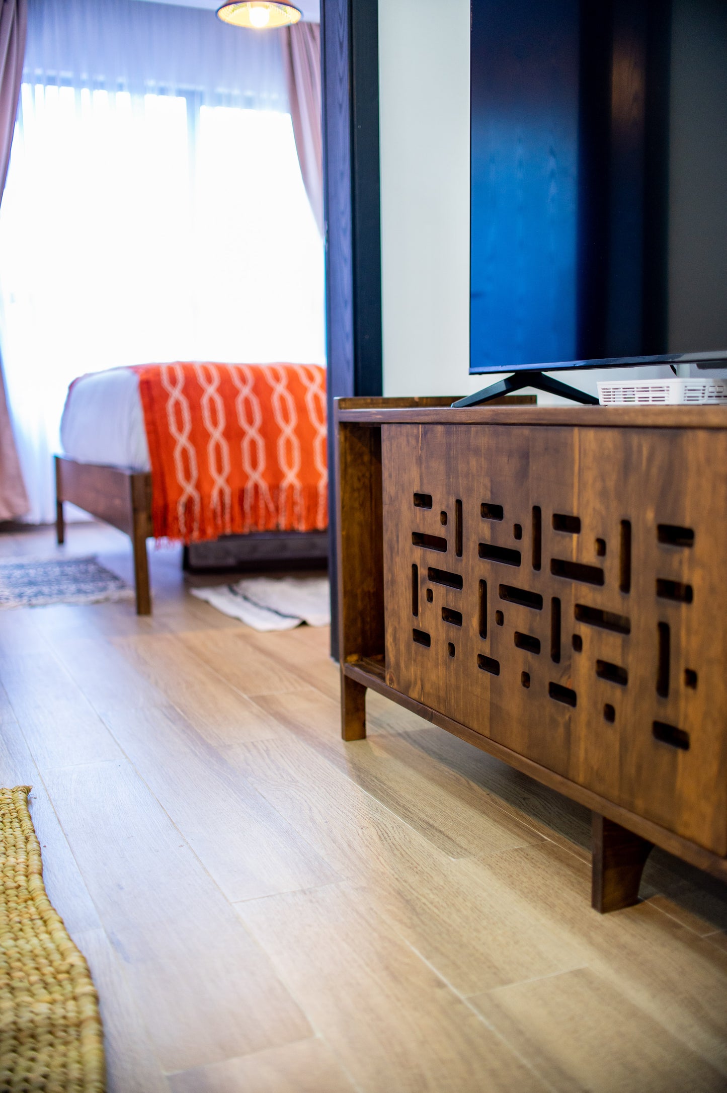 Wooden entertainment console with a television in a room with a bed and window.