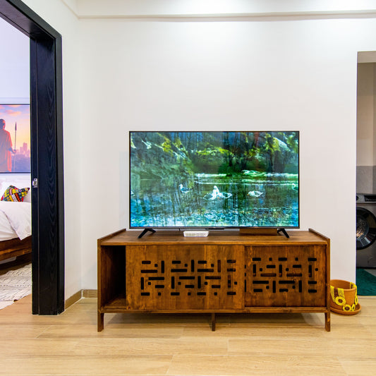 TV on a wooden stand in a living room with a bedroom and kitchen in the background.